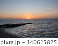 A calm sunset over the sea with a sandy shore and a breakwater 140615825