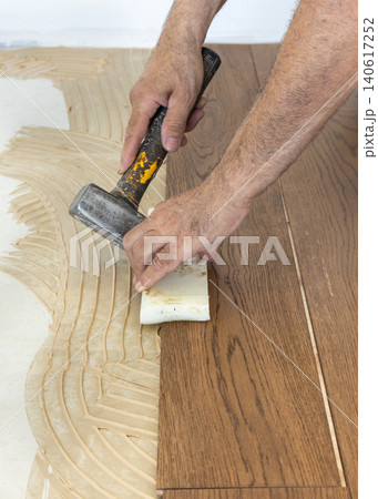 Carpenter fitting parquet planks over adhesive with hammer and tapping block, flooring installation Carpenter fitting parquet planks over adhesive with hammer and tapping block, flooring installation 140617252