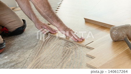 Carpenter installing herringbone wooden parquet planks during flooring work in apartment renovation Carpenter installing herringbone wooden parquet planks during flooring work in apartment renovation 140617264