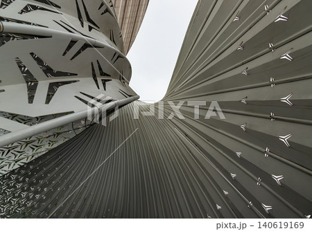 a dramatic low angle, this architectural detail highlights a futuristic dialogue between form, light, and texture. On the right, a massive, undulating surface of charcoal-grey ripples curves a dramatic low angle, this architectural detail highlights a futuristic dialogue between form, light, and texture. On the right, a massive, undulating surface of charcoal-grey ripples curves 140619169