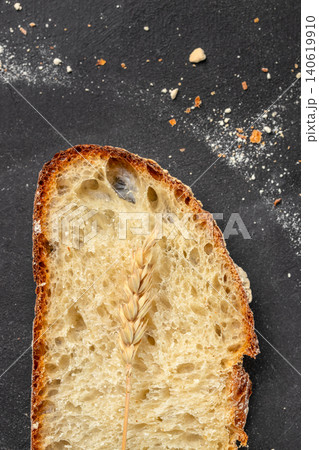 Slice of artisan sourdough bread with wheat spike on dark background, rustic bakery closeup Slice of artisan sourdough bread with wheat spike on dark background, rustic bakery closeup 140619910