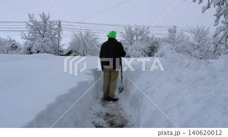 A man clearing deep snowdrifts after a heavy snowfall in a rural area or private property. The man is inside a deep, narrow trench he has cut in the snow A man clearing deep snowdrifts after a heavy snowfall in a rural area or private property. The man is inside a deep, narrow trench he has cut in the snow 140620012
