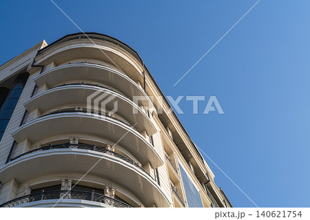 Bottom view of multi-storey building with round corner, panoramic balconies with 270-degree view against background of clear blue sky. Architectural elements in modern urban planning, building Bottom view of multi-storey building with round corner, panoramic balconies with 270-degree view against background of clear blue sky. Architectural elements in modern urban planning, building 140621754