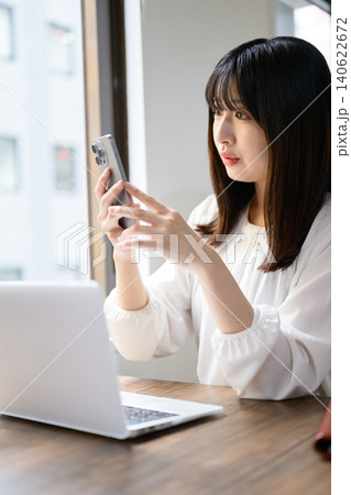 オフィスでノートパソコンとスマホを使って仕事をする日本人女性 オフィスでノートパソコンとスマホを使って仕事をする日本人女性 140622672