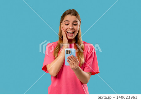 Shocked woman with smartphone on Blue studio with open mouth. Amazed lady, app Shocked woman with smartphone on Blue studio with open mouth. Amazed lady, app 140623963