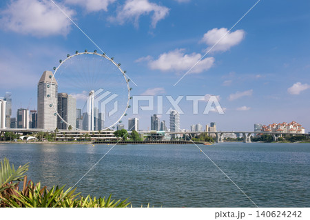 A scenic view of the Singapore skyline featuring the Singapore Flyer Ferris wheel, modern skyscrapers, and waterfront under a bright blue sky. The Marina Reservoir adds to the vibrant urban landscape A scenic view of the Singapore skyline featuring the Singapore Flyer Ferris wheel, modern skyscrapers, and waterfront under a bright blue sky. The Marina Reservoir adds to the vibrant urban landscape 140624242