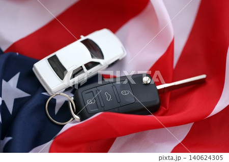 Ignition keys with remote control buttons and toy car on United States flag. Car driving in USA Ignition keys with remote control buttons and toy car on United States flag. Car driving in USA 140624305