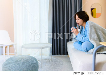 部屋で温かい飲み物を飲む女性 140625455