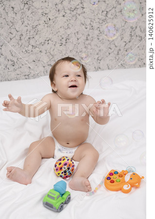 Adorable diaper baby boy sitting on white bed and reaching for toy Adorable diaper baby boy sitting on white bed and reaching for toy 140625912