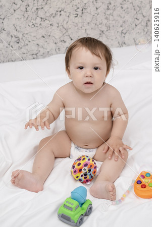 Adorable diaper baby boy sitting on white bed and reaching for toy Adorable diaper baby boy sitting on white bed and reaching for toy 140625916