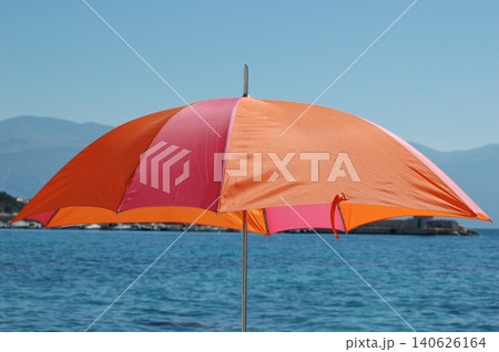Bright orange and pink beach umbrella against blue sea water 140626164