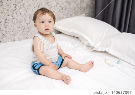 Cute baby boy in tank top sitting on bed and scratching his head thoughtfully Cute baby boy in tank top sitting on bed and scratching his head thoughtfully 140627097