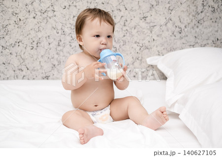 Cute shirtless baby boy holding a baby bottle with milk or formula on bed Cute shirtless baby boy holding a baby bottle with milk or formula on bed 140627105