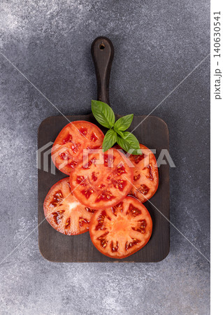 Sliced red summer tomato and basil on cutting board Sliced red summer tomato and basil on cutting board 140630541