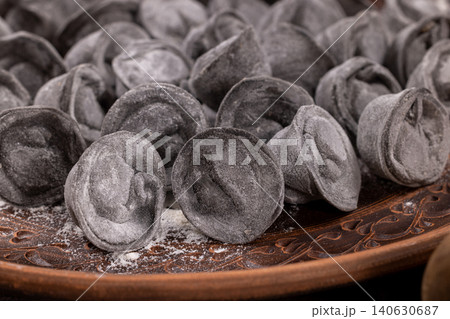 Uncooked black pelmeni on a rustic brown plate Uncooked black pelmeni on a rustic brown plate 140630687