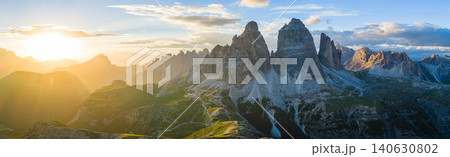Panoramic view of Tre Cime di Lavaredo glowing in golden sunset light in the Italian Dolomites. Dramatic alpine landscape with rugged peaks, winding trails and breathtaking scenery. 140630802