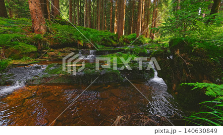 Crystal clear forest stream flowing through lush green woodland. Peaceful natural landscape with moss covered rocks, fresh water and tranquil wilderness atmosphere. Crystal clear forest stream flowing through lush green woodland. Peaceful natural landscape with moss covered rocks, fresh water and tranquil wilderness atmosphere. 140630849