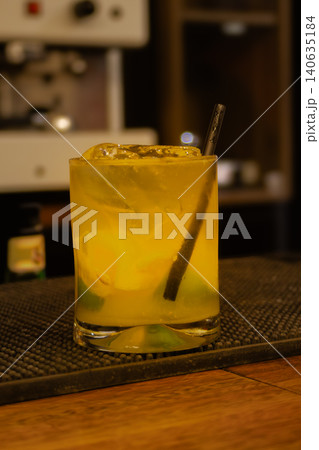Yellow cocktail with ice and a straw on a wooden bar counter, chilled and ready for an evening aperitif or celebration 140635184
