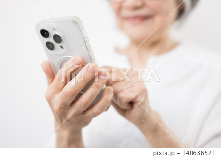 白背景でスマートフォンを見る操作、タップする笑顔のグレイヘアのシニア女性 登録や買い物、顔無しバナー 140636521