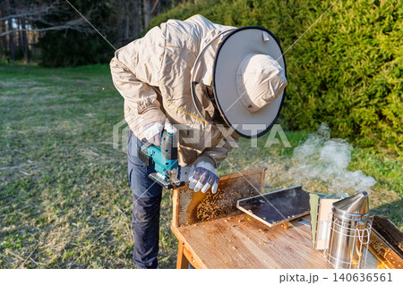 Beekeeper using electric tool to harvest honey from wooden frame in Netherlands garden setting Beekeeper using electric tool to harvest honey from wooden frame in Netherlands garden setting 140636561