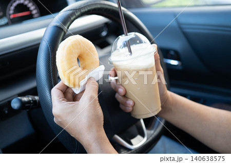 Asian woman driver hold ice coffee cup and sandwich bread for eat and drink in car, dangerous and risk an accident. Asian woman driver hold ice coffee cup and sandwich bread for eat and drink in car, dangerous and risk an accident. 140638575