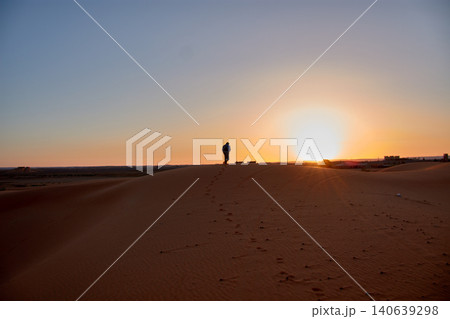 Silhouette of a tourist exploring the golden dunes under the warm light of the setting sun in Merzouga, Morocco Silhouette of a tourist exploring the golden dunes under the warm light of the setting sun in Merzouga, Morocco 140639298