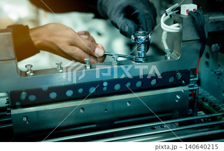 Mechanic technician hand fixing industrial machinery in factory. Professional technician service and maintenance packing machine equipment. Worker use wrench maintenance industrial machinery in plant. 140640215