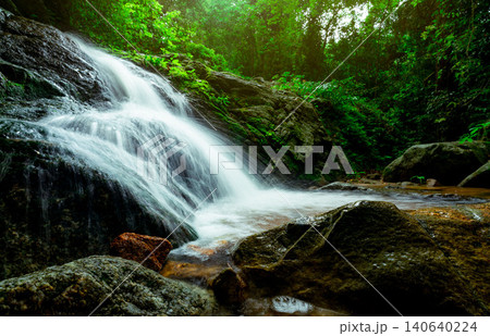 Beautiful waterfall in jungle. Waterfall in tropical forest with green tree and sunlight. Waterfall is flowing in jungle. Nature background. Rock or stone at waterfall. Long exposure photography. 140640224