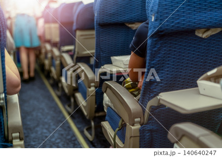 Passenger inside economy seat of commercial airplane. Plane cabin interior. Blur stewardess or air hostess walking in aircraft aisle for passenger service. People travel by plane with crowded flight. Passenger inside economy seat of commercial airplane. Plane cabin interior. Blur stewardess or air hostess walking in aircraft aisle for passenger service. People travel by plane with crowded flight. 140640247