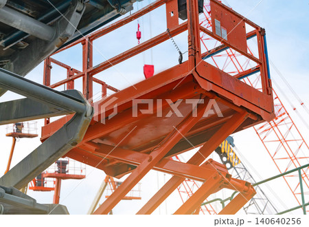 Articulated orange boom lift. Aerial platform lift. Telescopic boom lift against the blue sky. Maintenance and repair hydraulic boom lift service concept. Crane dealership background. Articulated orange boom lift. Aerial platform lift. Telescopic boom lift against the blue sky. Maintenance and repair hydraulic boom lift service concept. Crane dealership background. 140640256