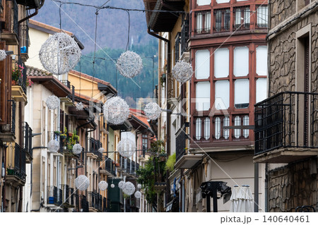 Narrow European village street decorated with hanging ornamental lights between historic buildings and balconies. Traditional old town architecture with scenic mountain background and peaceful travel. Narrow European village street decorated with hanging ornamental lights between historic buildings and balconies. Traditional old town architecture with scenic mountain background and peaceful travel. 140640461