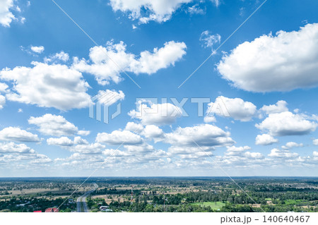 Blue sky with white cumulus clouds above a rural landscape. Natural weather patterns. Climate, nature, environmental sustainability and scenic outdoor landscapes. Peaceful weather conditions. Blue sky with white cumulus clouds above a rural landscape. Natural weather patterns. Climate, nature, environmental sustainability and scenic outdoor landscapes. Peaceful weather conditions. 140640467