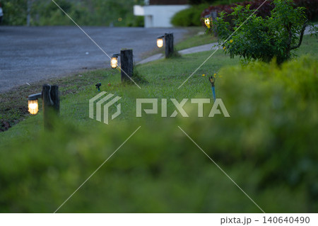 Garden pathway lighting along a landscaped lawn at dusk, decorative outdoor lamps. Illumination for residential property, hospitality design. Sustainable living. Resort environment and relaxing. Garden pathway lighting along a landscaped lawn at dusk, decorative outdoor lamps. Illumination for residential property, hospitality design. Sustainable living. Resort environment and relaxing. 140640490