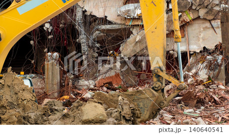 Excavator demolishing damaged concrete building at urban demolition site. Heavy construction machinery for redevelopment, excavation and infrastructure reconstruction project. Industrial construction. Excavator demolishing damaged concrete building at urban demolition site. Heavy construction machinery for redevelopment, excavation and infrastructure reconstruction project. Industrial construction. 140640541