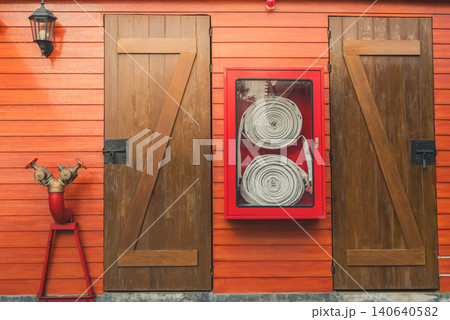 Fire hose in red cabinet hanging on orange wooden wall. Fire emergency equipment box for safety and security system. Fire safety pump. Deluge system of firefighting system. Plumbing fire protection. 140640582