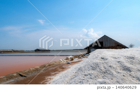 Landscape of brine salt farm with blue sky on sunny day. Salt warehouse. Pile of organic sea salt. Raw material of salt industrial. Sodium chloride mineral. Evaporation of sea water. Iodine. 140640629