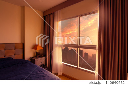 Bedroom in the morning with morning sunlight through glass window with opened curtains. Luxury bed in modern apartment in the city. Bedroom interior. Blue blanket covered bed. View from glass window. 140640682