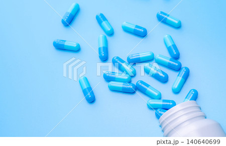 Blue capsule pills spread out of bottle on blue background. Pharmaceutical industry. Drug development and new drug research for treatment emerging Infectious diseases. Capsule pills industry. Blue capsule pills spread out of bottle on blue background. Pharmaceutical industry. Drug development and new drug research for treatment emerging Infectious diseases. Capsule pills industry. 140640699