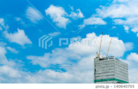 Construction site with tower crane lifting equipment beside a steel and concrete building. Real estate development, engineering progress and urban infrastructure growth. Construction industry. Construction site with tower crane lifting equipment beside a steel and concrete building. Real estate development, engineering progress and urban infrastructure growth. Construction industry. 140640705