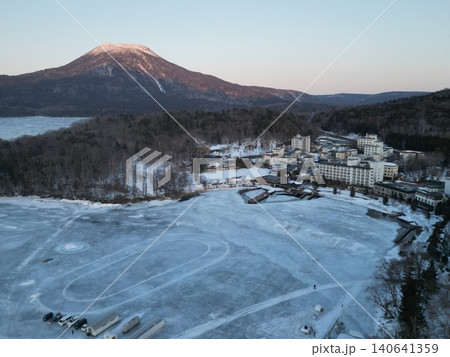 結氷した阿寒湖の湖畔の温泉街と阿寒岳の夕景の空撮 結氷した阿寒湖の湖畔の温泉街と阿寒岳の夕景の空撮 140641359