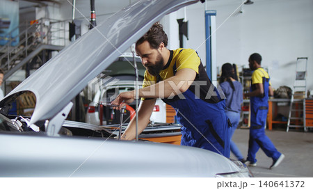 Licensed repairman in car service picks torque wrench from work station bench, using IT to tighten bolts after replacing engine. Licensed repairman in car service picks torque wrench from work station bench, using IT to tighten bolts after replacing engine. 140641372