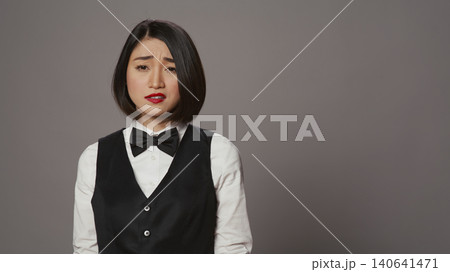 Bored receptionist being confused and overworked in studio, posing with confusion and fatigue over grey background, Asian administrator feeling uncertain and unsure about something. 140641471