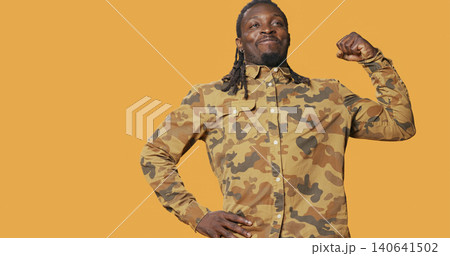 Athletic strong man flexing his biceps muscles on camera, advertising fitness routine and wellbeing. Athletic strong man flexing his biceps muscles on camera, advertising fitness routine and wellbeing. 140641502