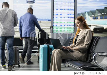 Business trip, woman CEO traveling abroad, in airport terminal, for global business negotiations, preparing to board international flight. Traveler in formal wear using laptop before departure. Business trip, woman CEO traveling abroad, in airport terminal, for global business negotiations, preparing to board international flight. Traveler in formal wear using laptop before departure. 140641606