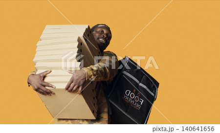 Young deliveryman giving huge stack of pizza boxes to client, delivering big fast food order and carrying takeaway backpack, with male model posing as delivery person with takeout food. 140641656