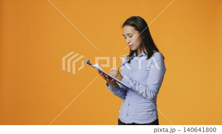 Filipino model writes information on files with clipboard, taking notes to create full report in front of camera, with young adult in casual clothing filling in documents, keeping track of something. Filipino model writes information on files with clipboard, taking notes to create full report in front of camera, with young adult in casual clothing filling in documents, keeping track of something. 140641800