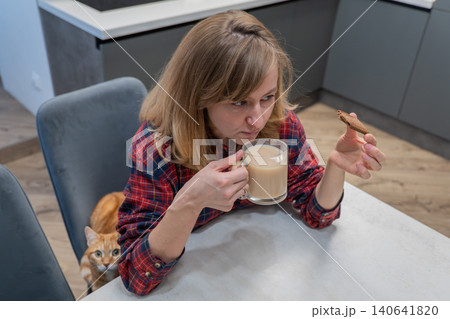 Preparing for online teaching session, Female prepares for internetbased lesson sipping her coffee peacefully, Woman relaxes with latte as she gets ready for digital teaching in small kitchen 140641820