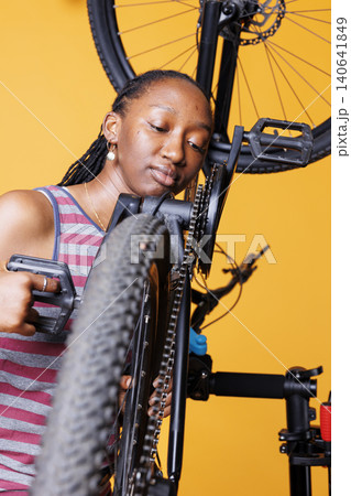 Woman closely analyzing bicycle chain with dedicated woman closely analyzing bike chain stay to maintain cycle efficiency. Woman closely analyzing bicycle chain with dedicated woman closely analyzing bike chain stay to maintain cycle efficiency. 140641849