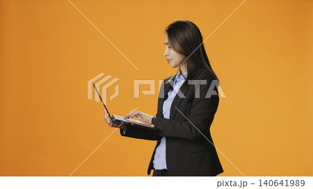Businesswoman browsing sites on laptop in studio, looking for inspiration or research on portable computer against orange background, with girl checking webpages on internet, search engine. 140641989