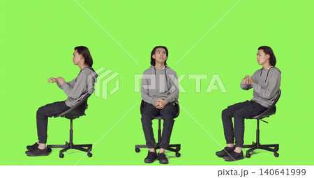 Young man looks at wristwatch and waiting in studio, acting impatient while sitting on chair over full body green screen, with agitated person checking time on watch, trying to stay positive. Young man looks at wristwatch and waiting in studio, acting impatient while sitting on chair over full body green screen, with agitated person checking time on watch, trying to stay positive. 140641999